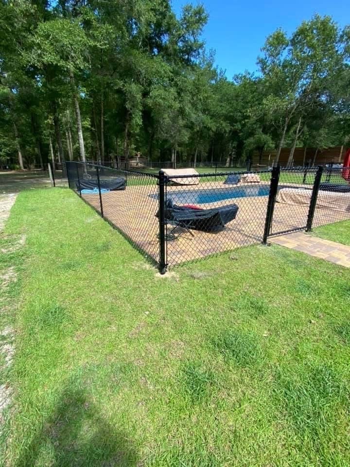 Fenced dog park with shaded area under trees and green grass, featuring play equipment and benches for pet owners