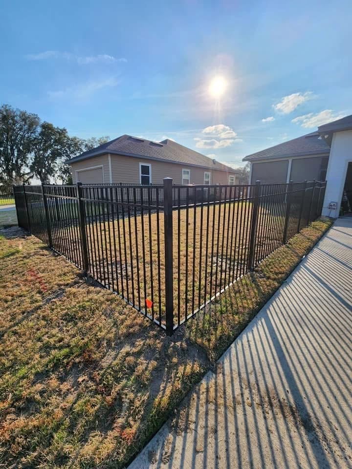 Black metal fence surrounding residential home with open yard and metal shed on sunny day