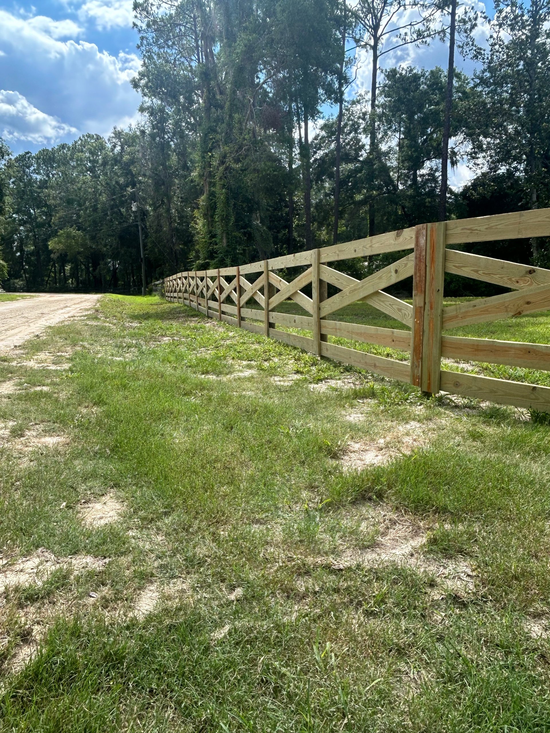 Long wooden ranch fence with X-pattern rails stretching through a grassy field